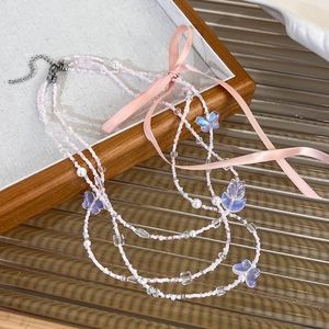 Detail of multi-layer beaded necklace featuring pink silk ribbons and butterfly pendants