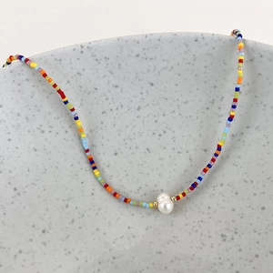 Detail of colorful beaded necklace with freshwater pearl on a minimalist ceramic edge