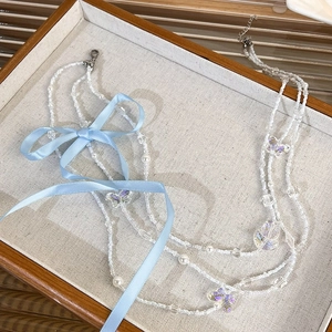 Detail of layered beaded necklace with blue ribbon bows and butterfly pendants on a tray