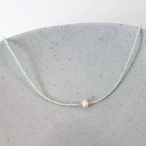 Close-up of handmade green beaded necklace featuring a white freshwater pearl and gold beads