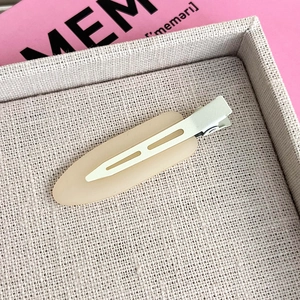 Macro shot of a minimalist light beige matte duckbill hair clip on a textured tray