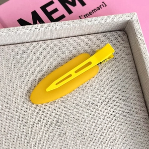 Close-up of matte yellow hair clip on a beige woven tray with soft lighting