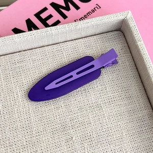 Close-up of deep purple matte duckbill hair clip on a textured beige tray display