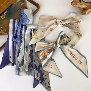 Detailed macro of narrow silk twilly scarves with artistic landscape prints on white table