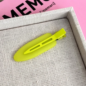 Close-up of a matte neon yellow duckbill hair clip on a textured display tray