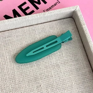 Close-up of a matte peacock green duckbill hair clip on a minimalist display tray