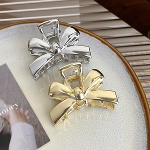 Detail view of gold and silver metallic bow hair claws with polished finish and anti-slip teeth