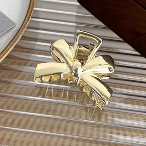 Macro shot of a golden metal bow hair claw clip showing polished mirror finish and spring