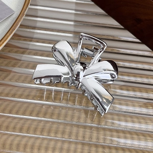 Detailed view of a silver bow hair claw clip with a polished mirror finish on textured glass