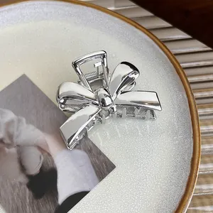 Detail of silver metallic bow hair claw clip with a glossy mirror finish on a ceramic plate