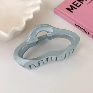 Detail of grey-blue wavy acrylic hair claw clip with glossy finish on decorative tray