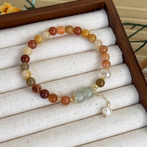 Dettaglio di bracciale con perle di agata rossa e ciondolo di giada verde su velluto