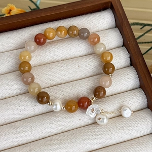 Dettaglio del bracciale con perle di pietre dure multicolore e ciondolo a fiore bianco
