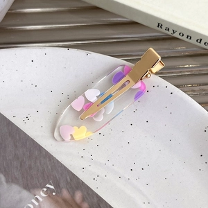 Detail of transparent heart hair clip filled with colorful sequins on a ceramic tray