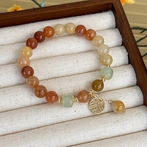 Dettaglio del bracciale multistrato con perline, ciondolo dorato Fu e nappina a fiore