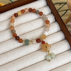 Dettaglio del bracciale di perline con ciondolo a fiore e giada verde su velluto bianco