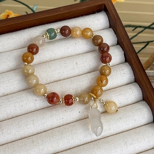 Dettaglio del bracciale di perline con ciondolo arachide su velluto bianco