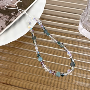 Detail of crystal beads and floral charm mobile strap on ribbed glass surface