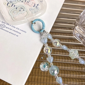 Détail de perles de cœur bleues irisées et de charmes à paillettes sur dragonne de téléphone