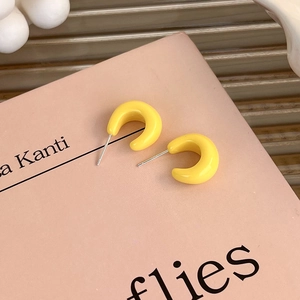 Detail of bright yellow dopamine style C-shaped acrylic earrings on decorative pink plate
