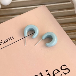 Close-up of light blue C-shaped stud earrings with smooth enamel finish and metal posts