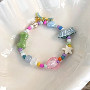 Close-up of colorful beaded bracelet with heart and star charms in a white ceramic bowl