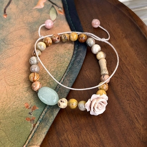 Macro detail of natural stone beads with a carved pink rose and green jade charm