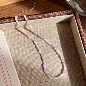 Détail du collier de perles colorées avec tubes argentés sur un plateau tressé