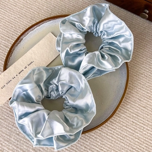Detailansicht von zwei hellblauen plissierten Satin-Haargummis auf einem Teller