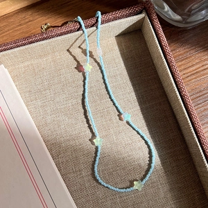 Détail d'un collier de perles bleu clair avec breloques étoiles colorées dans son coffret