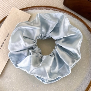 Detailansicht eines cremeblauen Satin-Haargummis mit Lagenfalten und Seidentextur