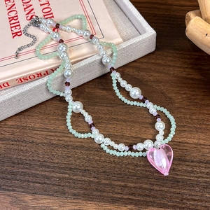 Détail du collier à deux rangs avec pendentif cœur rose posé sur des livres anciens
