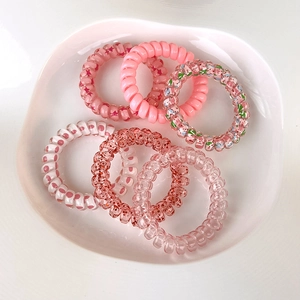 Dettaglio di sei elastici per capelli a spirale nei toni del rosa su un vassoio bianco