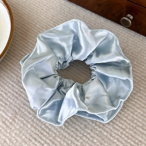 Detailansicht des cremeweißen Satin-Haargummis mit doppellagigem, gewelltem Kantenabschluss