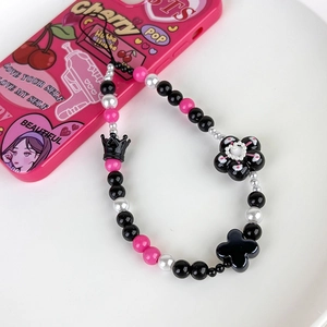 Detailed close-up of Y2K phone strap with black crown and pink beads on white tray