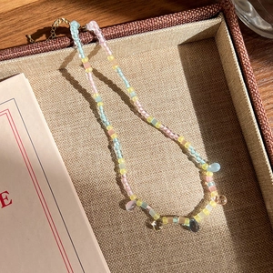 Détail d'un collier de perles colorées avec pendentifs gouttes dans un écrin brun
