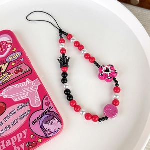 Cute Y2K phone charm with black crown, pink flower, and beaded strap on a white plate
