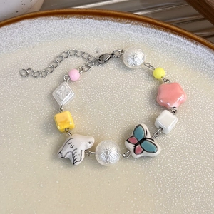 Détail du bracelet en céramique colorée avec papillon et perles sur un plat blanc