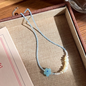 Gros plan du collier perlé avec fleur bleue et perles irrégulières sur un plateau tressé