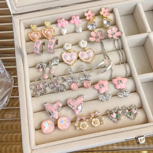 Detail view of pink enamel heart and flower earrings with shiny crystals in a jewelry box