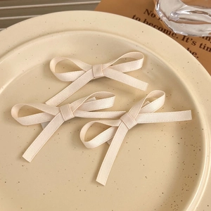Close-up of three cream-white ribbon bow hair clips on a decorative ceramic tray