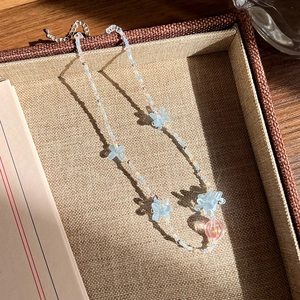 Détail du collier de perles avec papillons bleus et pendentif boule rose sur plateau tressé