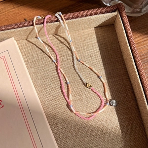 Détail du collier de perles avec perles roses et pendentif floral argenté