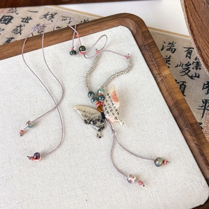 Macro detail of a butterfly necklace with ink painting, calligraphy, and beaded purple cord