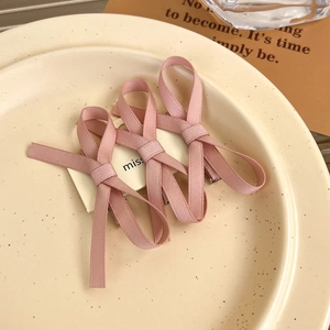Detailed view of three pink ribbon bow hair clips on a white card in a cream-colored setting