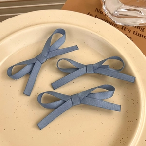 Close-up of three dusty blue ribbon bow hair clips on a vintage ceramic plate