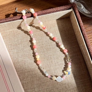 Gros plan d'un collier de perles roses avec des breloques cœur et ours sur un plateau décor