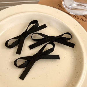 Detailed shot of three black ribbon bow hair clips on a cream ceramic plate