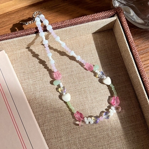 Détail d'un collier de perles colorées avec motifs de cœurs et fleurs dans une boîte