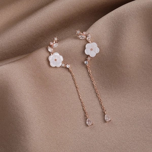 Detailed shot of floral shell earrings with rose gold chains and teardrop zircon pendants